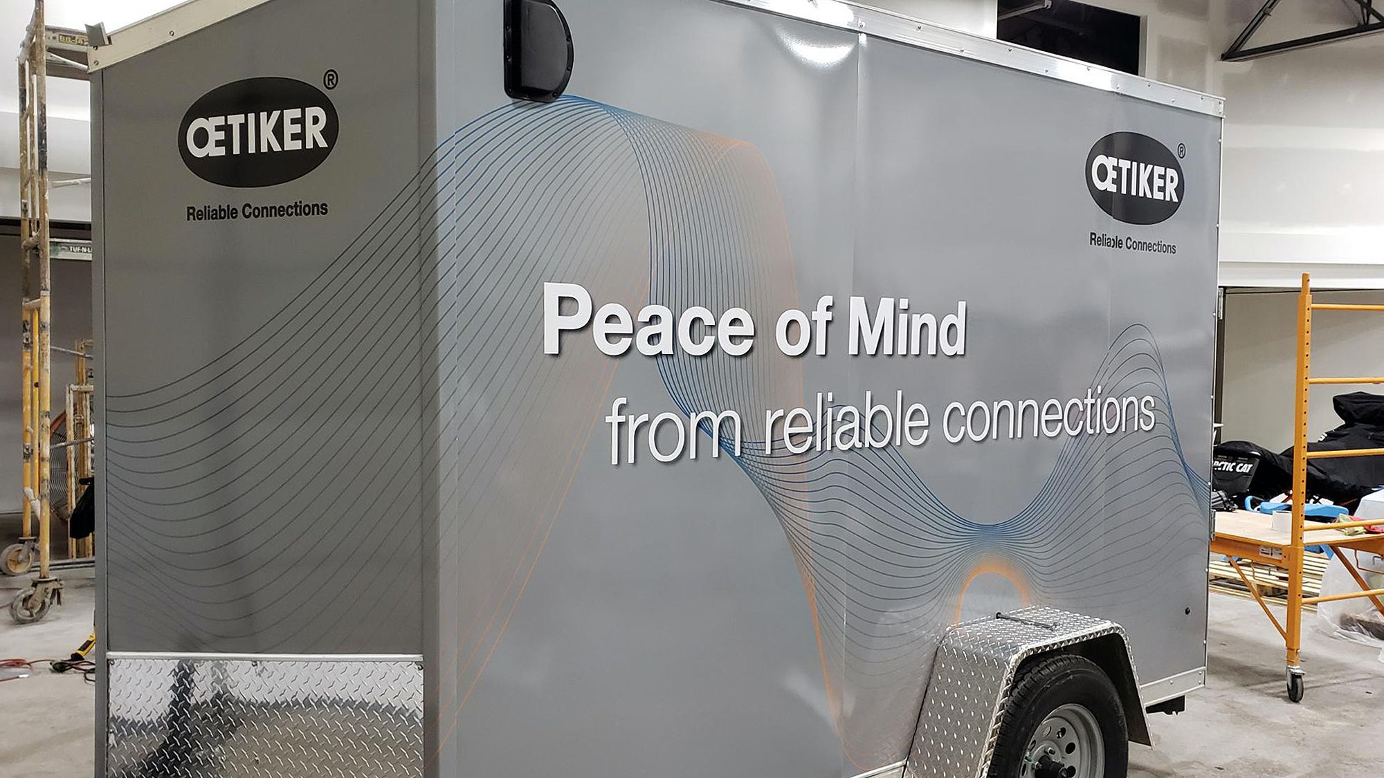 A commercial trailer with a custom vinyl wrap with gray, white, and black shapes and logos.