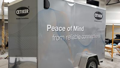 A commercial trailer with a custom vinyl wrap with gray, white, and black shapes and logos.
