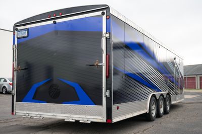 A snowmobile trailer with a custom vinyl wrap with white, blue, and black shapes and lines.