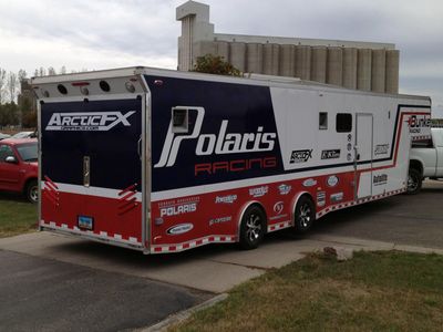 A snowmobile trailer with a custom vinyl wrap with white, blue, and red stripes and logos.