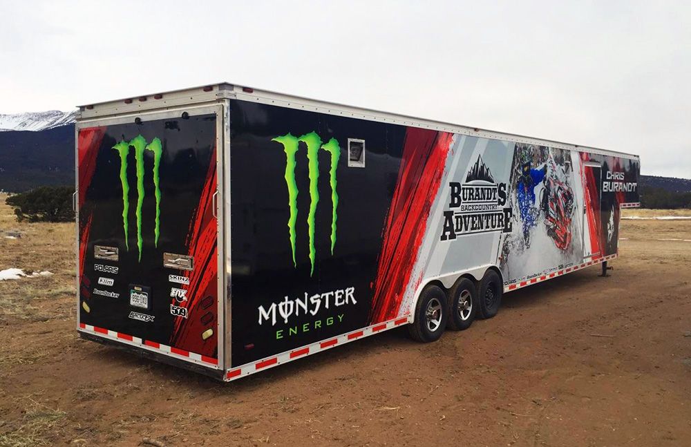 A snowmobile trailer with a custom vinyl wrap with red, white, and black shapes and logos.