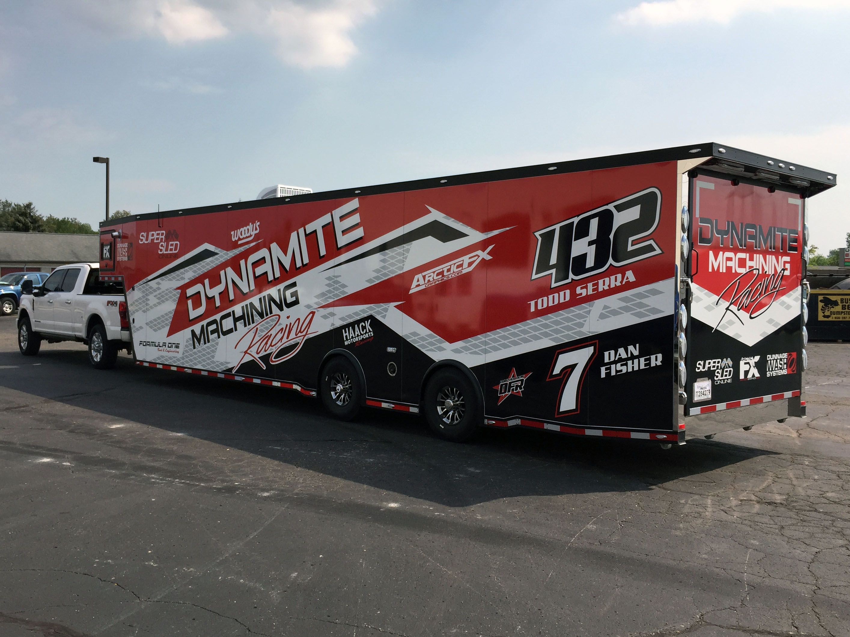 A snowmobile trailer with a custom vinyl wrap with black, red, and white shapes and patterns.