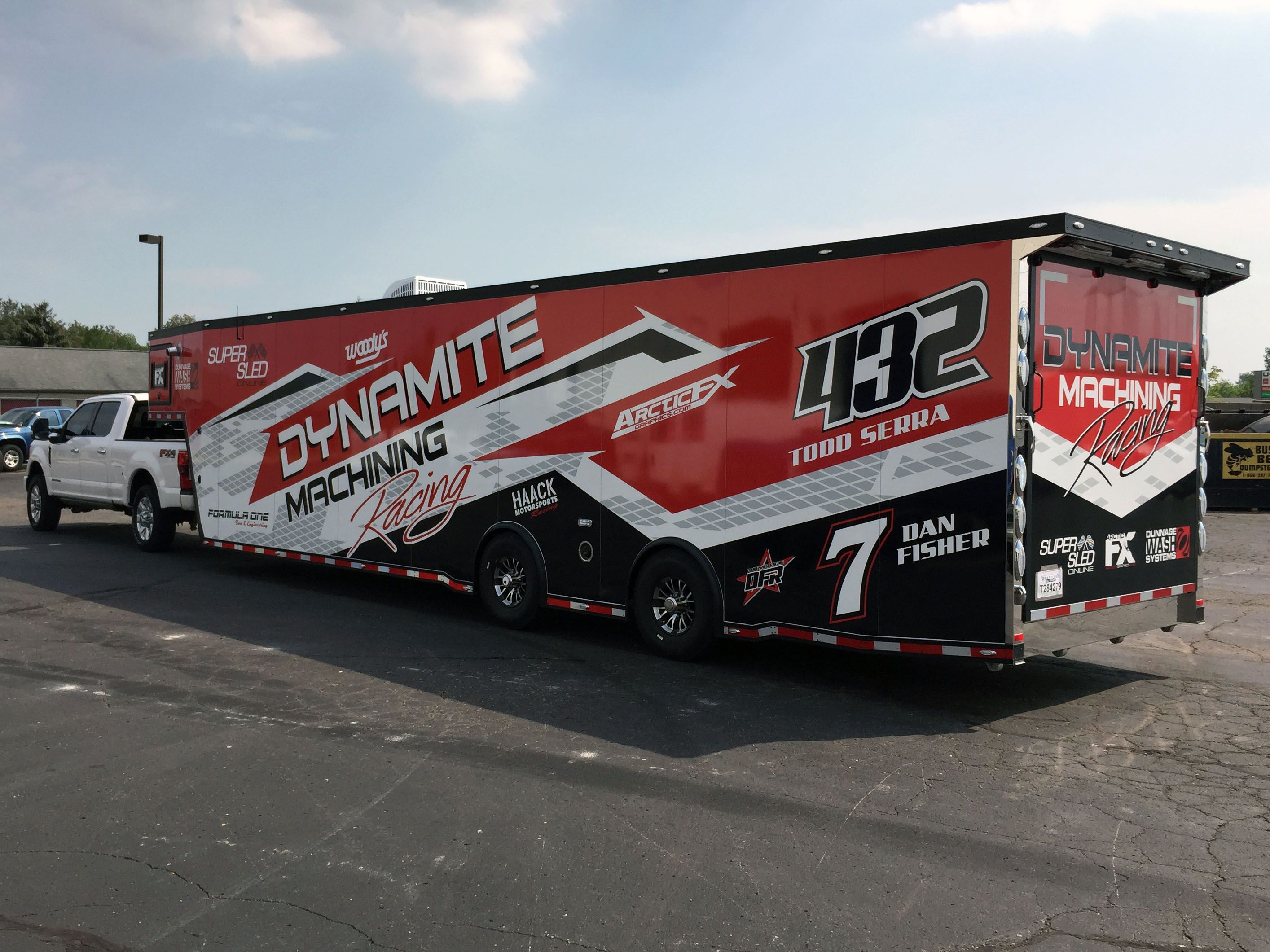 A snowmobile trailer with a custom vinyl wrap with black, red, and white shapes and patterns.