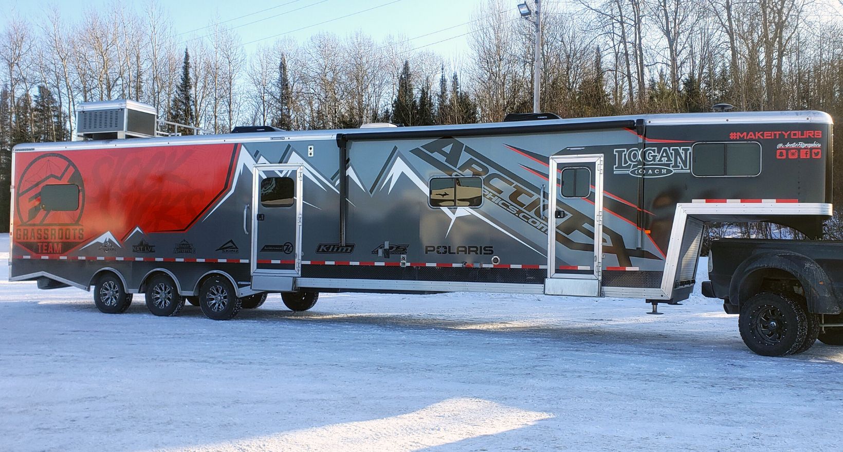 A snowmobile trailer with a custom vinyl wrap with red, black, and gray mountains and shapes.
