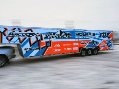 A snowmobile trailer with a custom vinyl wrap with bright orange, white and blue shapes and lines.