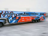 A snowmobile trailer with a custom vinyl wrap with bright orange, white and blue shapes and lines.