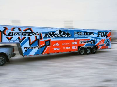 A snowmobile trailer with a custom vinyl wrap with bright orange, white and blue shapes and lines.