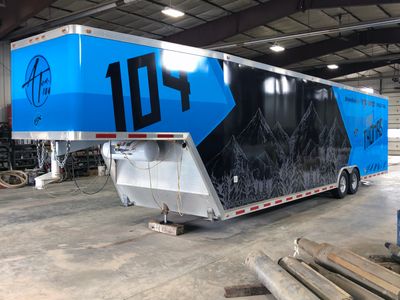 A snowmobile trailer with a custom vinyl wrap with blue, black, and gray sketch mountains and shapes.
