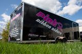 A snowmobile trailer with a custom vinyl wrap with pink ribbon riders logo and white text.