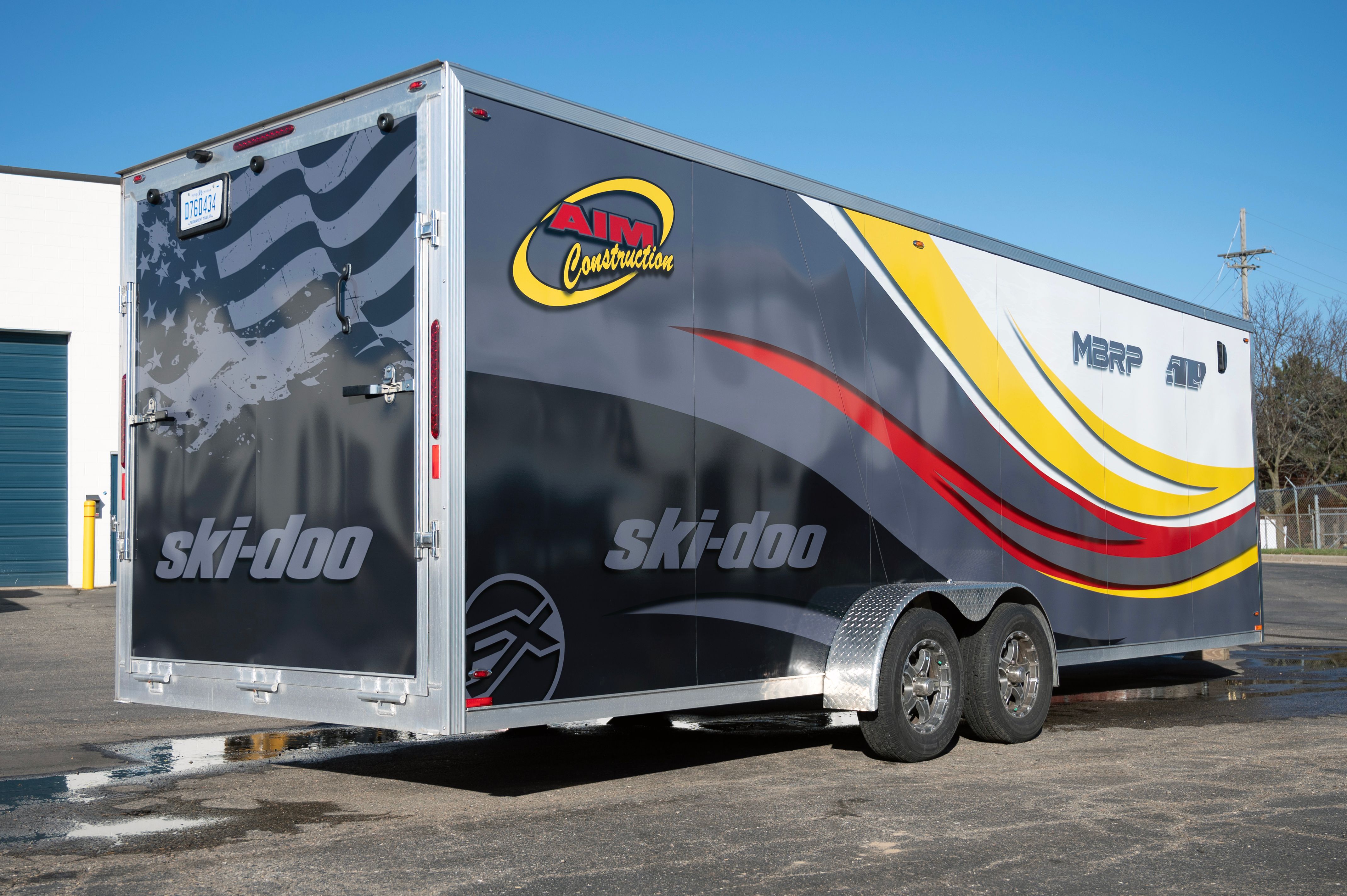 A snowmobile trailer with a custom vinyl wrap with yellow, white, gray and black tribal lines and swirls.
