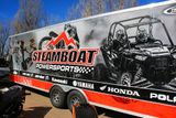 A snowmobile trailer with a custom vinyl wrap with red, white, and black lines and photographs.