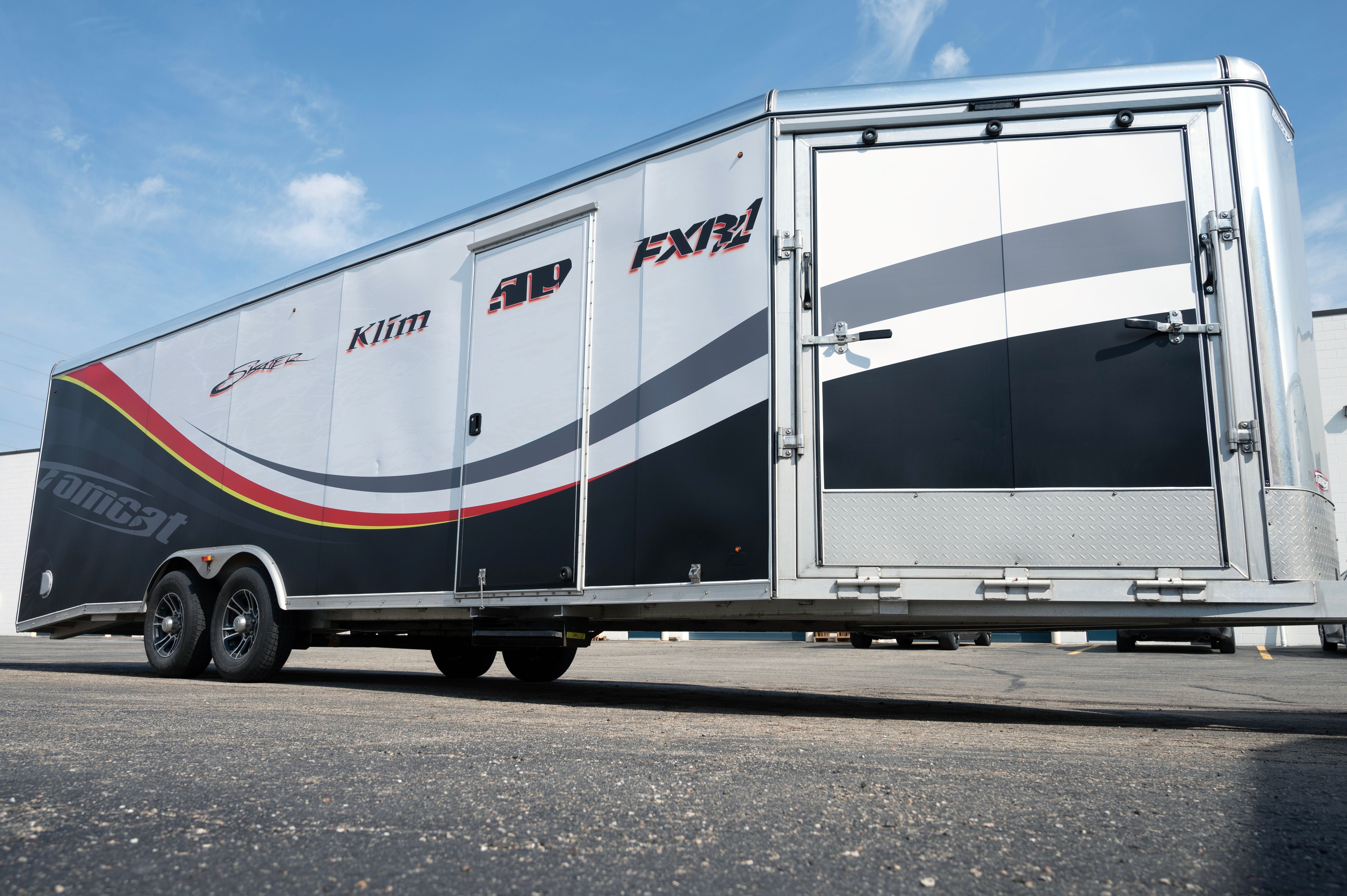 A snowmobile trailer with a custom vinyl wrap with yellow, white, gray and black lines and swirls.