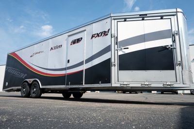 A snowmobile trailer with a custom vinyl wrap with yellow, white, gray and black lines and swirls.
