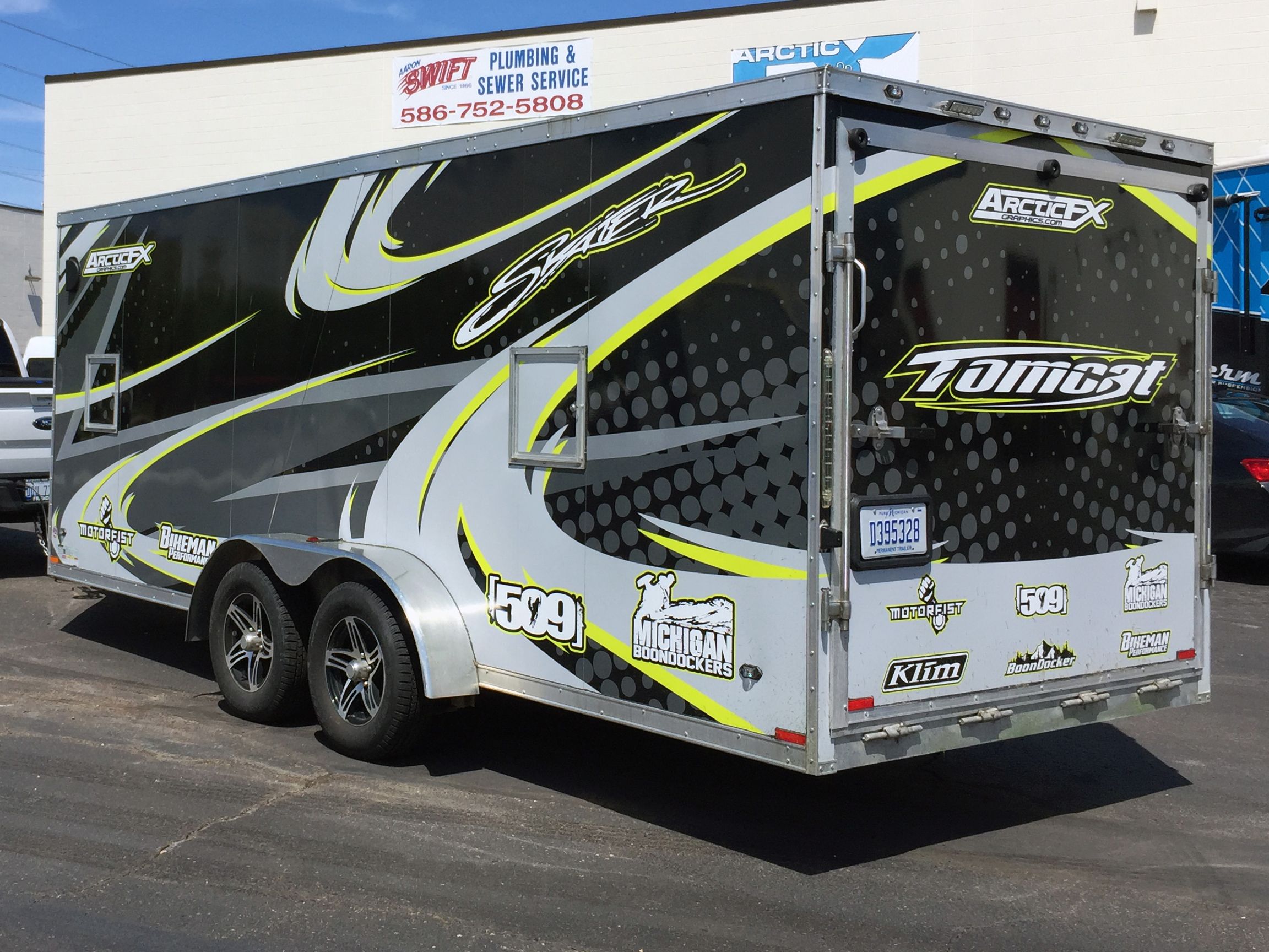 A snowmobile trailer with a custom decorative tribal vinyl wrap with lime, gray and black lines and swirls.