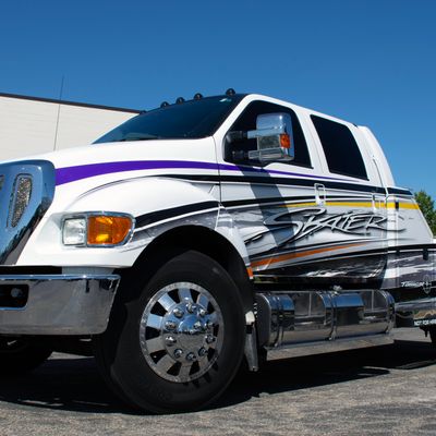 A commercial work truck with a custom vinyl wrap with purple, white, and black logos and text with a stripe design
