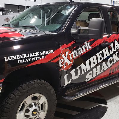 A commercial work truck with a custom vinyl wrap with red, white, and black logos and text with a grunge design