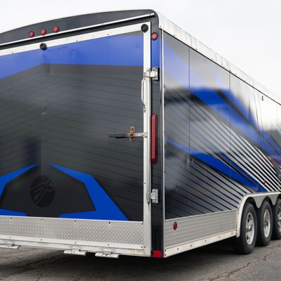 A snowmobile trailer with a custom vinyl wrap with white, blue, and black shapes and lines.